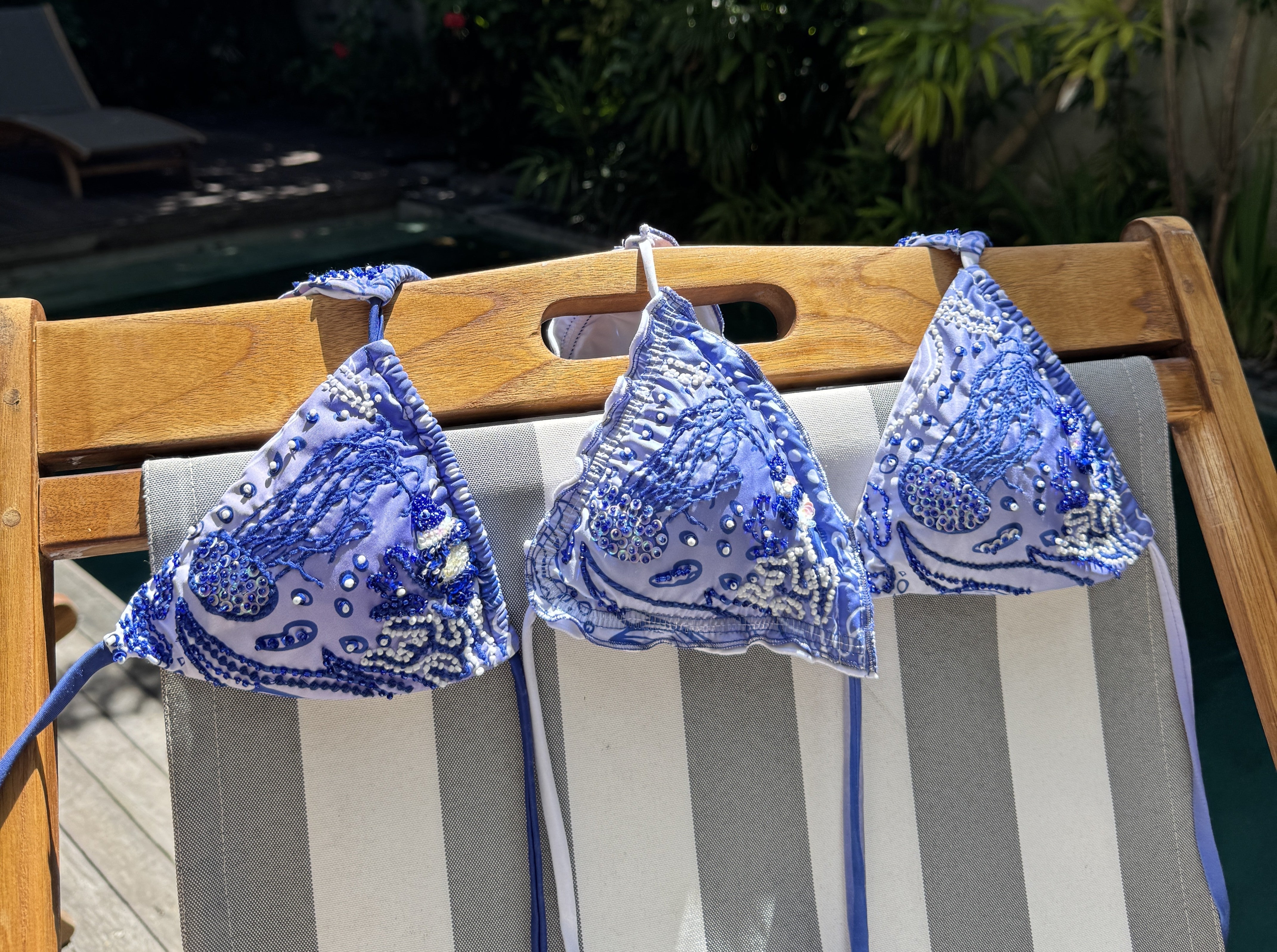 three triangle bikinis hanging over the top of a wooden sun bed