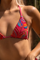 Close-up of a woman wearing the Zahora Red bikini top with colorful tribal pattern decorated with embroidery and beadwork, blurred background