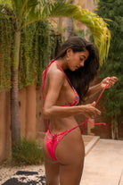 Woman wearing Zahora Red bikini set with colorful tribal patterns decorated with embroidery and beadwork standing outdoors with tropical greenery in the background.